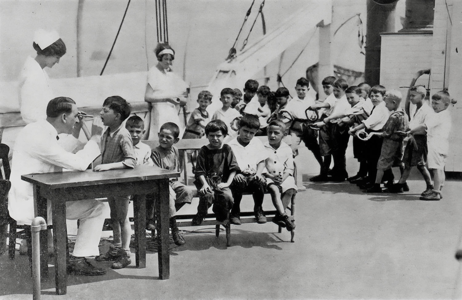 Doctor checking a line of boys on deck, 1920s